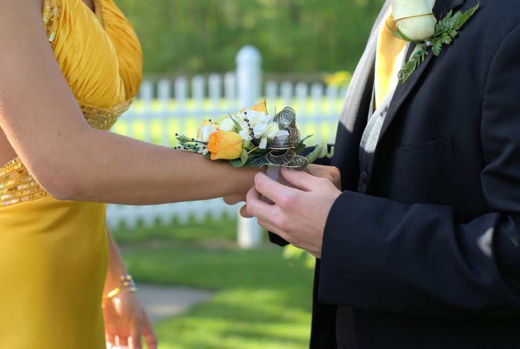 man placing flowers on woman's wrist for prom